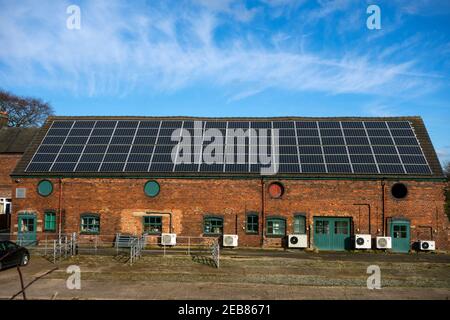 Große Reihe von Solarzellen auf dem Dach eines Bauernhauses und Luftwärmepumpe entlang der Wand beide mit alternativen grünen Energie-Technologie Stockfoto