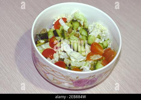Gemüsebeilage aus gehackten Tomaten, Gurken, grünen Erbsen aus der Dose, mit peking-Kohlblättern, in einer Porzellanschüssel mit Muster Stockfoto