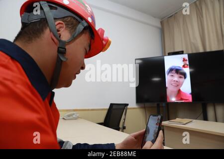 (210212) -- JINCHANG, 12. Februar 2021 (Xinhua) -- Bergmann Xin Chao hat einen Video-Chat mit seiner Mutter, bevor er unterirdisch in der dritten Bergbauzone der Jinchuan-Gruppe in Jinchang, nordwestlich von Chinas Provinz Gansu, am 11. Februar 2021 arbeitet. In der dunklen Mine in einer Tiefe von mehr als 600 Metern brüllen die Bergbaumaschinen und das Erz auf dem Förderband erstrahlt in metallischem Glanz. Es ist die dritte Bergbauzone der Jinchuan-Gruppe in Jinchang, einer der wichtigsten Produktionsstandorte des Landes für Nickel, Kobalt und Kupfer. Arbeiter hier, die während des Frühlingsfestes nicht nach Hause kamen, blieben an ihren Posten bei e Stockfoto