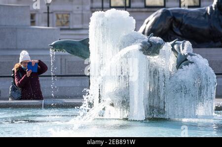 Die Menschen schauen auf einen gefrorenen Brunnen am Trafalgar Square in London, während der kalte Schnapper weiterhin einen Großteil der Nation in ihren Griff zieht. Bilddatum: Freitag, 12. Februar 2021. Stockfoto