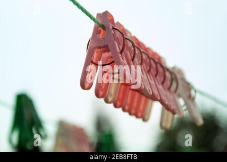 Farbige Wäscheklammern Kunststoff, mit Metallringen als Klammern. Hängen auf grünen Wäscheleine aus Kunststoff Garn, im Freien. Selektiver Fokus Stockfoto