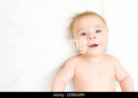 Glücklich neugeborenen Jungen mit einem großen Lächeln. Liebenswert Baby liegt auf weißem Hintergrund, kopieren Raum. Lustige Kind Kleinkind mit blau grauen Augen und Ingwer Haar l Stockfoto