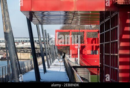 Touristen fotografieren auf dem verschneiten Tor im Parc de la Villette in Paris 19th unter leuchtend roten Metallstrukturen namens "folies". Stockfoto