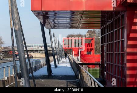 Zwei Frauen, die auf dem verschneiten Tor im Parc de la Villette in Paris 19th unter leuchtend roten Metallstrukturen namens 'folies' spazieren. Stockfoto