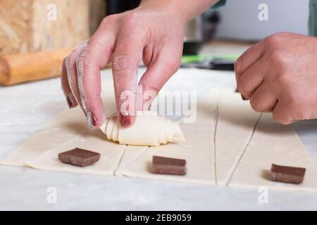 Die Hände der Frau arbeiten mit Blätterteig und machen Croissants mit Schokolade. Stockfoto