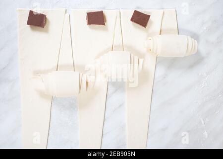 Herstellung von Croissants mit Schokolade, auf einem weißen Küchentisch. Stockfoto
