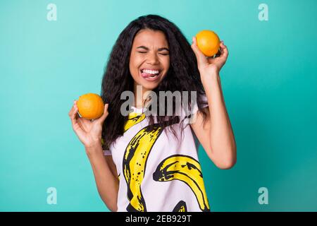 Foto von jungen schwarzen Mädchen halten zwei Orangen Zunge heraus Viel Spaß tragen Banana Print T-Shirt isoliert teal Farbe Hintergrund Stockfoto