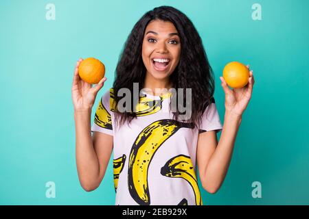 Foto von schwarzen Mädchen halten zwei Orangen offenen Mund Blick Kamera tragen Banana Print T-Shirt isoliert türkisfarbenen Hintergrund Stockfoto