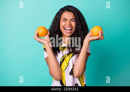 Foto von niedlichen schwarzen Mädchen halten zwei Orangen offenen Mund Augen geschlossen tragen Banana Print T-Shirt isoliert türkisfarbenen Hintergrund Stockfoto