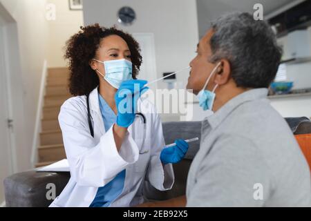 Ältere gemischte Rasse Mann mit weiblichen Arzt zu Hause Besuch tragen Gesichtsmasken, die einen Abstrichtest durchführen Stockfoto