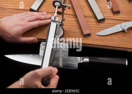 Hände schärfen ein japanisches Messer mit Damaskus Stahl mit einem Manuelle Maschine Stockfoto