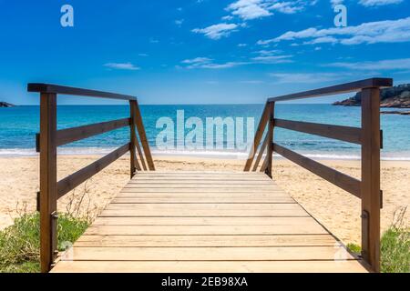 Promenade zum Sandstrand. Holzsteg über Sand zum Meer. Sonniger Strand mit Holzfußböden. Urlaub Hintergrund. Sommerurlaub Konzept. Kopieren Sie den SPAC Stockfoto