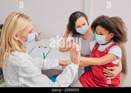 Afroamerikanisches Kind mit ihrer Mutter, die bei der Hausarztkonsultation Schutzmasken trägt. Globale Pandemie Stockfoto