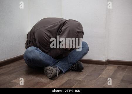 Verzweifelter junger Drogenabhängiger trägt Kapuze und sitzt allein in der Ecke. Konzept der Traurigkeit, depressiv und Lebensprobleme Stockfoto