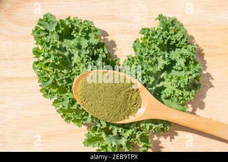 Grünes Grünkohlpulver im Holzlöffel Hintergrund Blatt auf Holztisch. Stockfoto