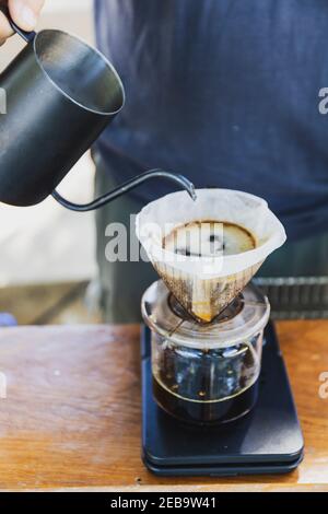 Barista verschüttet heißes Wasser Bereiten Sie gefilterten Kaffee aus Edelstahl Teekanne zu tropfen Papiermaschine auf schwarzen einfachen Gewichten. Alles dicke Holztabl Stockfoto