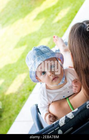 Mutter fürsorgliches Kind draußen auf der Veranda sitzen auf einem Liegestuhl, Baby suchen interessiert mit Angst Ausdruck Stockfoto