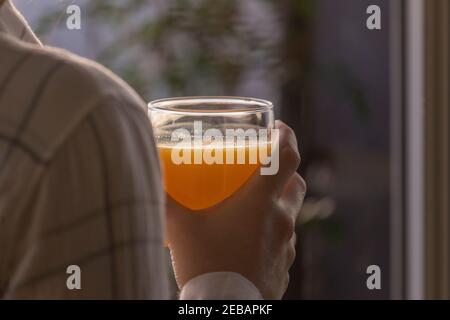 Eine junge Frau trinkt einen frisch und lecker gepressten Orangensaft, gesund und voller Vitamine, am Morgen, zu Hause, vor dem Frühstück und Stockfoto