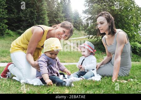 Zwei Freundinnen genießen ein Picknick in einer schönen sonnigen Tag mit ihren kleinen Töchtern - Frauen sitzen mit kleinen Kleine Mädchen auf Gras im Berg Stockfoto