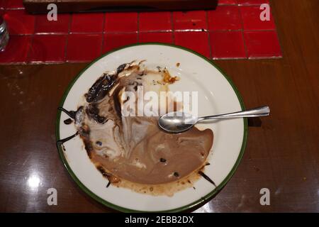 Draufsicht auf geschmolzenes Schokoladeneis auf einem weißen Teller mit einem Löffel mit verschwommenem Hintergrund. Stockfoto
