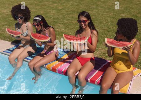 Eine Gruppe von Freundinnen, die Wassermelone essen und am Pool sitzen. Im Sommer kann man sich im Freien entspannen. Stockfoto
