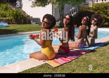 Eine Gruppe von Freundinnen, die Wassermelone essen und am Pool sitzen. Im Sommer kann man sich im Freien entspannen. Stockfoto
