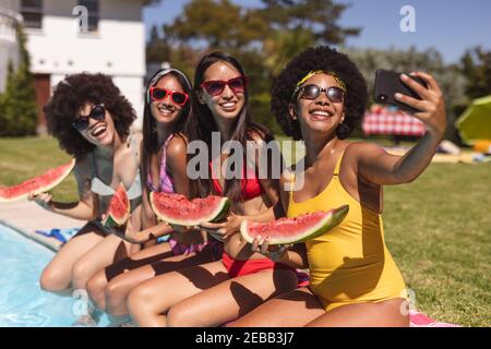 Eine vielfältige Gruppe von Freundinnen, die Selfie mit Wassermelone am Pool machen. Im Sommer kann man sich im Freien entspannen. Stockfoto