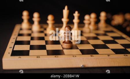 Nahaufnahme von weißen und schwarzen Schachfiguren aus Holz an Bord. Selektiver Fokus auf Konfrontation von schwarzen Bauern gegenüber weißen König und Königin mit Bauern auf c Stockfoto