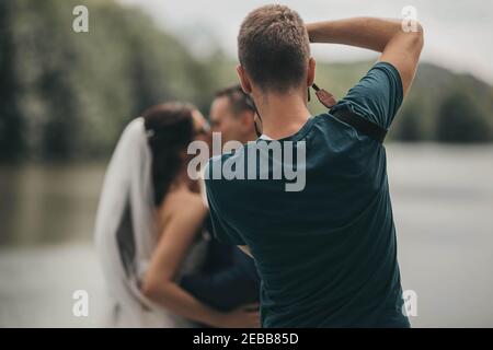 Flacher Fokus eines männlichen Fotografen, der Bilder von einem Frisch verheiratetes küssendes Paar Stockfoto