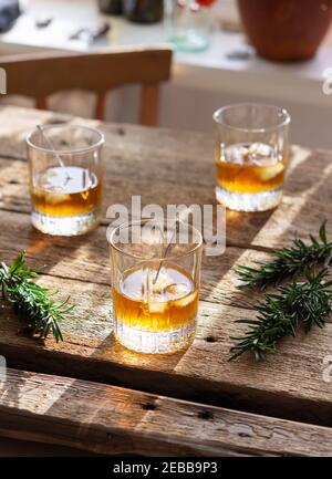 Starker Alkoholiker in Gläsern in der Sonne, Whiskey oder Gin mit Eis auf Holzgrund Stockfoto