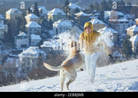 Junger Mann mit Hund im Winter. Haustierbesitzer mit seinem labrador Retriever spielt im Schnee gegen die Stadt. Prag, Tschechische Republik Stockfoto