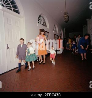 Geburtstagsfeier für Caroline Kennedy und John F. Kennedy, Jr.. First Lady Jacqueline Kennedy geht mit ihrem Sohn John F. Kennedy, Jr. (hält seine motheru0027s Hand), während einer gemeinsamen Geburtstagsparty für John, Jr. und Caroline Kennedy. Ostflügelkorridor, Weißes Haus, Washington, D.C. Stockfoto