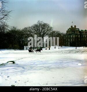 First Lady Jacqueline Kennedyu0027s (JBK) Schlittenfahrt auf dem South Lawn. First Lady Jacqueline Kennedy und nicht identifizierte Kinder fahren über den South Lawn in einem offenen Schlitten gezogen von Caroline Kennedyu0027s Pony Macaroni. Das Executive Office Building ist rechts zu sehen. Weißes Haus, Washington, D.C. [Flecken an der unteren linken und rechten Ecke des Bildes sind original auf das Negative.] Stockfoto