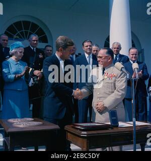 Übergabe der Distinguished Service Medal an General George H. Decker, 12:05pm Uhr. Präsident John F. Kennedy schüttelt die Hände mit dem scheidenden Stabschef der US-Armee, General George H. Decker (rechts), nachdem er ihm die Distinguished Service Medal (DSM) überreicht hatte. Im Hintergrund (L-R): Stellvertretender Verteidigungsminister, Roswell L. Gilpatric; Helen Decker; Chef der Naval Operations, Admiral George W. Anderson, Jr.; stellvertretender Kommandant des Marine Corps, LT. General John C. Munn; Senator Stuart Symington von Missouri (teilweise versteckt); Verteidigungsminister, Robert S. McNamara; General Stockfoto
