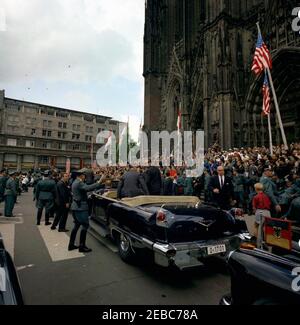 Europareise: Deutschland, Köln: Autokolonne, Dom. Präsident John F. Kennedy (Mitte links, im Hintergrund) steht in einem offenen Cabrio, nachdem er den Kölner Dom (Kuf6lner Dom) verlassen hat, wo er die Messe besuchte. Bundeskanzler Konrad Adenauer steht links von Präsident Kennedy; Sonderassistent des Präsidenten, Kenneth P. Ou2019Donnell (zurück zur Kamera), sitzt im Auto im Vordergrund. Ebenfalls im Bild: Militärhilfe für den Präsidenten, General Chester V. Clifton; westdeutscher Botschafter in den Vereinigten Staaten, Karl Heinrich Knappstein; Geheimagent des Weißen Hauses, Gerald A. U Stockfoto