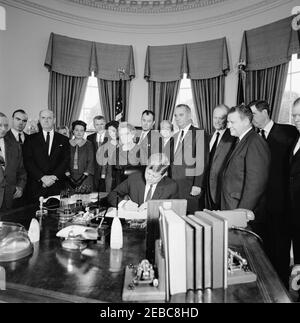 Unterzeichnungszeremonie, Senat Gemeinsame Resolution 133 Öffentliches Recht 87-702, Sam Rayburn Medaille, 12:20pm. Präsident John F. Kennedy (sitzt an der Rezeption) unterzeichnet eine gemeinsame Resolution des Senats, um eine Gedenkmedaille zu Ehren des verstorbenen Präsidenten des Repräsentantenhauses, Sam Rayburn (Texas), zu genehmigen. Stehend (L-R): Repräsentant Clark W. Thompson; Repräsentant James C. Wright, Jr.; Repräsentant Walter Rogers; ehemalige Mitarbeiter des verstorbenen House Speaker, Jack Neathery und Lorraine Kimbrough; Assistent des Secretary of the Treasury, Robert A. Wallace; ehemaliger Berater des verstorbenen House Speaker, Bernice Frazier; Long Stockfoto