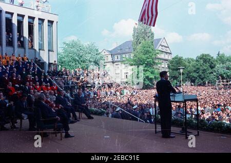 Europareise: Deutschland, West-Berlin: Präsident Kennedy spricht vor der Freien Universität, 3:30pm Uhr. Präsident John F. Kennedy (rechts, stehend an Mikrofonen) hält Bemerkungen an der Freien Universität Berlin in West-Berlin (Bundesrepublik). Auf der linken Bühne sitzen unter anderem: Bundeskanzler Konrad Adenauer, Bürgermeister Willy Brandt, Sprecher des Berliner Abgeordnetenhauses Otto Bach, Rektor der Freien Universität Ernst Heinitz, französischer Kommandant in Berlin, Generalmajor Edouard Toulouse; Direktor des Radio im amerikanischen Sektor (RIAS) in Berlin und Übersetzer für Stockfoto