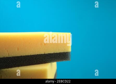 Gelb kombinierte schwarze Scheuerschwämme Schwämme isoliert mit blauem Hintergrund. Haushalt, Küche, Fahrzeuge Putze oder jedes Reinigungskonzept. Stockfoto