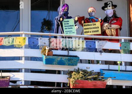 Sythen, Münsterland, NRW, 12th. Februar 2021. Eine Familie hat im kleinen Dorf Sythen bei Haltern-am-See in Nordrhein-Westfalen eine Szene mit gekleideten Shop-Dummies in Gesichtsmasken und positiven Ermutigungen zum "Bleiben optimistisch" auf ihrem Balkon inszeniert. Kredit: Imageplotter/Alamy Live Nachrichten Stockfoto