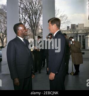 Mittagessen zu Ehren von Sylvanus Olympio, Präsident von Togo, 1:00pm Uhr. Präsident John F. Kennedy besucht mit Präsident von Togo, Sylvanus Olympio (links), nach der Ankunft von Präsident Olympiou2019s im Weißen Haus für ein Mittagessen zu seinen Ehren. Im Hintergrund stehen Fotografen, darunter Wochenschau-Fotograf für United Press Movietone, Thomas J. Craven, Sr., und Filmfotograf für Columbia Broadcasting System (CBS), Tom J. Craven, Jr.. North Portico, White House, Washington, D.C. Stockfoto