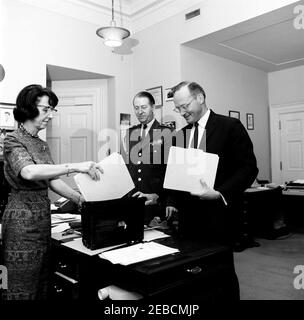 Mitarbeiter des Weißen Hauses: Militärhilfe für den Präsidenten Gen. Chester V. Clifton, nationaler Sicherheitsberater McGeorge Bundy, Präsidialsekretärin Evelyn Lincoln. Persönliche Sekretärin von Präsident John F. Kennedy Evelyn Lincoln (links) legt einen Aktenordner in Präsident Kennedyu0027s schwarz Alligator Aktentasche als Sonderassistent des Präsidenten für nationale Sicherheitsangelegenheiten McGeorge Bundy hält die Aktentasche offen. Military Aide to the President General Chester V. Clifton (Mitte) schaut auf. Büro Presidentu2019s Secretaryu2019s, Weißes Haus, Washington, D.C. Stockfoto