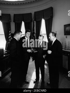Gedenken an die Hundertjahrfeier der Homestead Act, 12:08pm. Präsident John F. Kennedy nimmt ein Geschenk als Teil einer Gedenkfeier zum hundertjährigen Bestehen des Homestead Act, Oval Office, White House, Washington, D.C. Willis G. Scholl, Präsident des Farm Equipment Institute, und C.R. Gutermuth, Vizepräsident des Wildlife Management Institute, übergibt dem Präsidenten ein fußlanges Modell eines Stahlpfluges. Innenminister Stewart Udall steht auf der linken Seite. Stockfoto