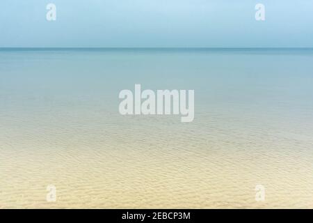 Beigefarbener Sandstrand und türkisfarbener, gewellter Meereshintergrund. Transparentes blaues Meerwasser über Sandstrand. Glänzendes, winkendes Meerwasser über dem Sandstrand. Summert Stockfoto