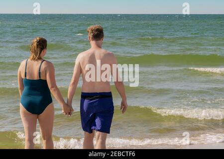 Pärchen, die sich zum Schwimmen in Wellen vorbereiten, spritzt das Meer. Frau und Mann halten die Hände zusammen und gehen ins Meer. Paar gehen in winkenden Meer schwimmen. Sommer vaca Stockfoto