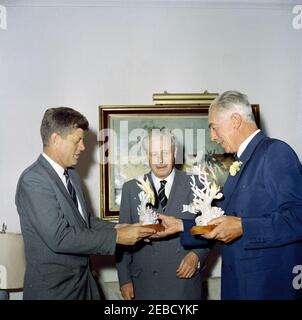 Reise nach Bermuda: Generalmajor Sir Julian Gascoigne, Gouverneur von Bermuda, überreicht Geschenke an Präsident Kennedy und Harold Macmillan, Premierminister von Großbritannien, im Government House, Hamilton, Bermuda. Präsident John F. Kennedy und Premierminister von Großbritannien Harold Macmillan (Mitte) erhalten Porzellanfiguren vom Gouverneur von Bermuda, Generalmajor Sir Julian Gascoigne (rechts), im Government House in Hamilton, Bermuda. President Kennedyu2019s Figur zeigt einen spanischen Hog-Fisch und einen Sergeant Major Fisch, der um ein Stück Koralle schwimmt; eine silberne Plakette auf der Basis lautet: u0022The Stockfoto