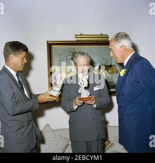 Reise nach Bermuda: Generalmajor Sir Julian Gascoigne, Gouverneur von Bermuda, überreicht Geschenke an Präsident Kennedy und Harold Macmillan, Premierminister von Großbritannien, im Government House, Hamilton, Bermuda. Präsident John F. Kennedy und Premierminister von Großbritannien Harold Macmillan (Mitte) erhalten Porzellanfiguren vom Gouverneur von Bermuda, Generalmajor Sir Julian Gascoigne (rechts), im Government House in Hamilton, Bermuda. President Kennedyu2019s Figur zeigt einen spanischen Hog-Fisch und einen Sergeant Major Fisch, der um ein Stück Koralle schwimmt; eine silberne Plakette auf der Basis lautet: u0022The Stockfoto