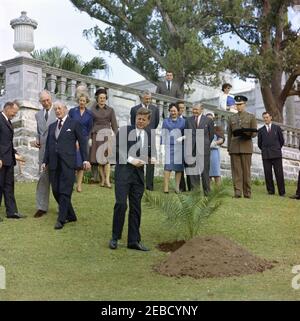 Ausflug nach Bermuda: Baumpflanzung im Government House, Hamilton, Bermuda. Präsident John F. Kennedy schneidet ein Band von einem neu gepflanzten Baum auf dem Gelände des Regierungshauses in Hamilton, Bermuda. L-R: Präsident Kennedyu2019s Sonderassistent für nationale Sicherheit McGeorge Bundy; Gouverneur von Bermuda Generalmajor Sir Julian Gascoigne; Premierminister von Großbritannien Harold Macmillan; Lady Gascoigne (Ehefrau des Gouverneurs); nicht identifiziert; Präsident Kennedy; mehrere nicht identifizierte Personen. Pierre Salinger, Pressesprecher des Weißen Hauses, blickt vom Balkon aus. Stockfoto