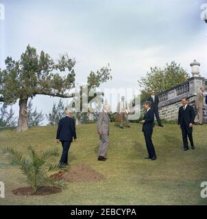 Ausflug nach Bermuda: Baumpflanzung im Government House, Hamilton, Bermuda. Präsident John F. Kennedy und andere stehen auf dem Gelände des Government House in Hamilton, Bermuda, während einer Baumbepflanzungszeremonie. L-R: Premierminister von Großbritannien Harold Macmillan (zurück zur Kamera); Gouverneur von Bermuda Generalmajor Sir Julian Gascoigne; Associate White House Press Secretary Andrew T. Hatcher; Präsident Kennedy; White House Secret Service Agent Ernest u201cErnieu201d Olsson; Präsident Kennedyu2019s Special Assistant for National Security McGeorge Bundy; nicht identifiziert. Stockfoto