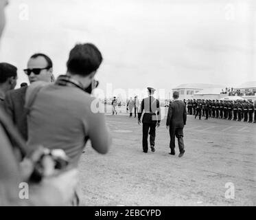 Reise nach Bermuda: Ankunft auf der Kindley Air Force Base, Bermuda, 12:55pm Uhr. Präsident John F. Kennedy (Mitte, Hintergrund) geht mit dem Gouverneur von Bermuda, Generalmajor Sir Julian Gascoigne, nach der Ankunft in Bermuda Presidentu2019s von Palm Beach, Florida. Pressevertreter stehen links, Militärangehörige rechts. Kindley Air Force Base, St. Davidu2019s Island, Bermuda. [Foto von Dan Lewis] Stockfoto