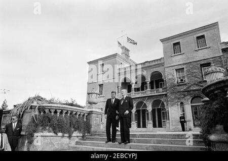 Ausflug nach Bermuda: Baumpflanzung im Government House, Hamilton, Bermuda. Präsident John F. Kennedy und Premierminister von Großbritannien Harold Macmillan stehen auf den Stufen des Regierungshauses in Hamilton, Bermuda. Links: Associate White House Press Secretary Andrew T. Hatcher; White House Secret Service Agent Arthur L. u201cArtu201d Godfrey. Stockfoto